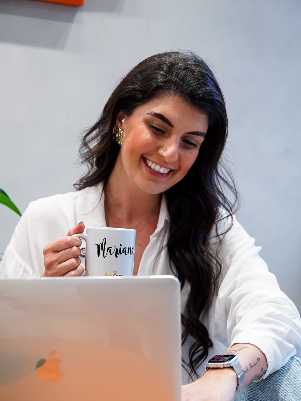 Mari trabalhando no notebook com uma caneca na mão