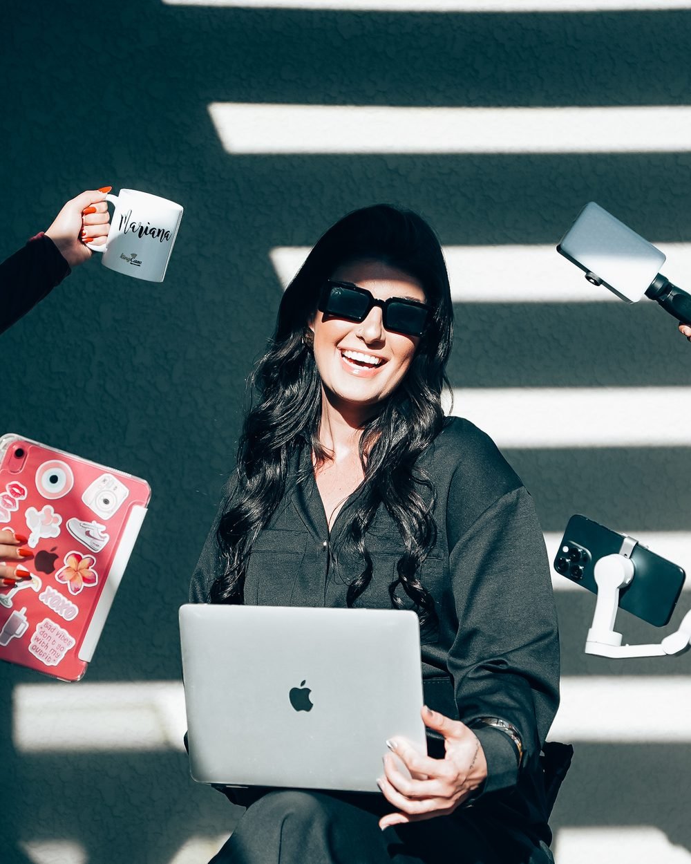 Mari trabalhando com notebook, celular e caneca em volta